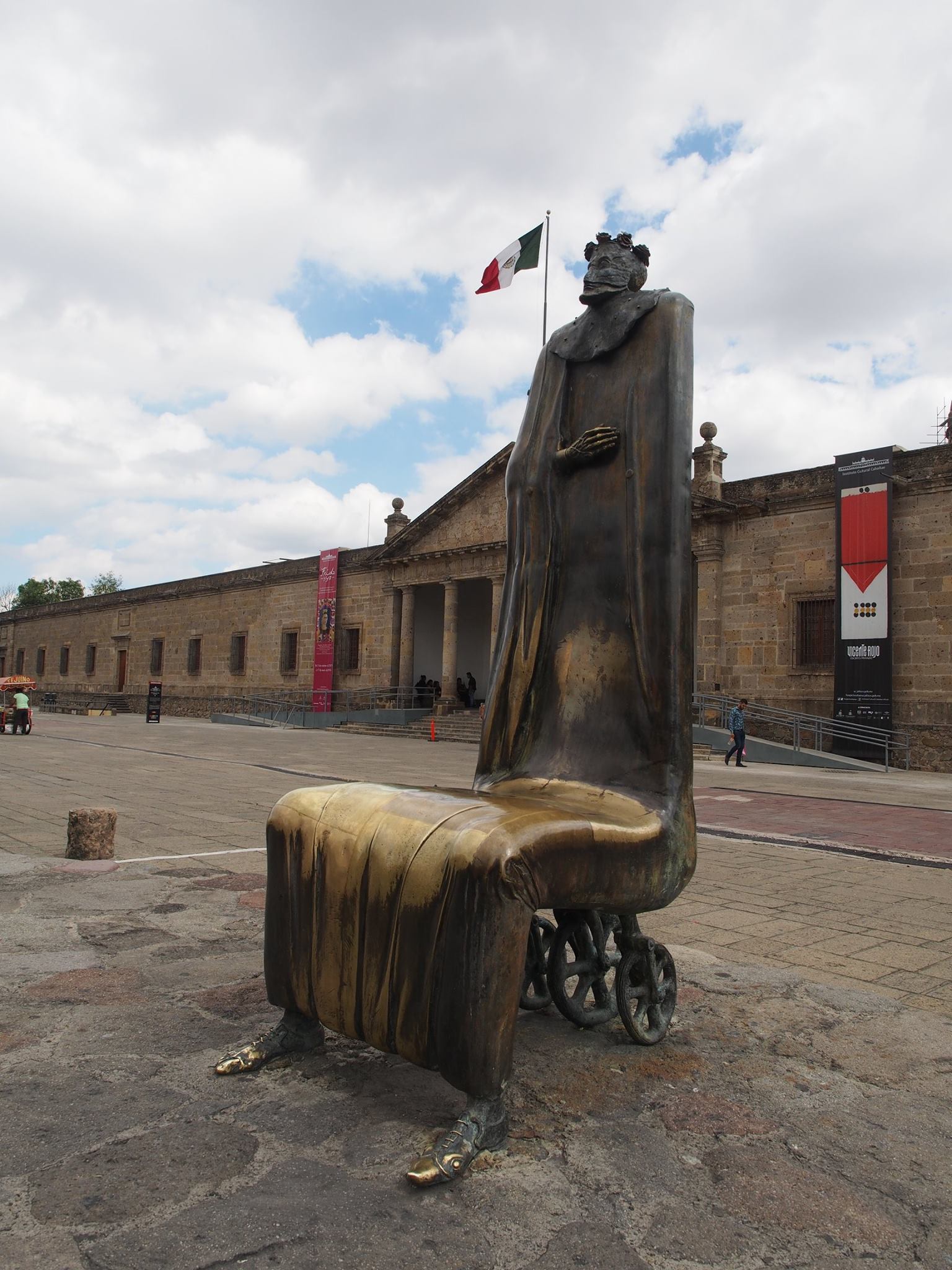 chair sculpture in front of mexican flag and building